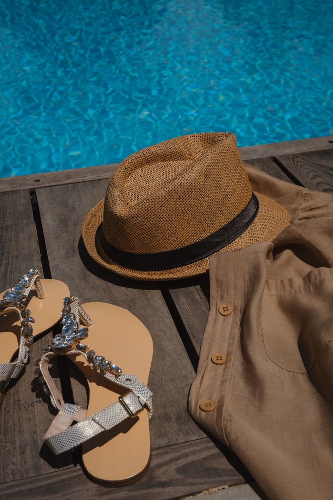Stylish summer essentials including hat, sandals, and shirt by the poolside.